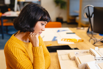 Biracial young female architect examining architectural model in creative office