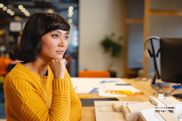 Thoughtful biracial young female architect with architectural model in creative office
