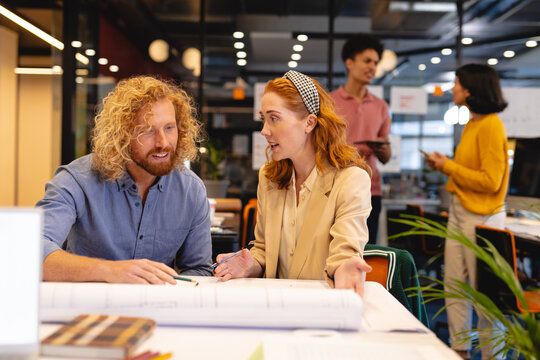 Caucasian businessman and businesswoman discussing over blueprint at desk in creative office