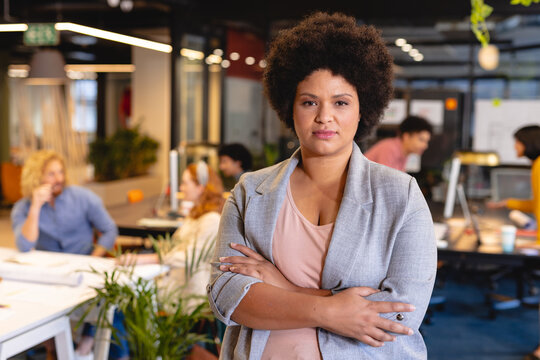 Portrait of confident biracial mid adult businesswoman standing with arms crossed at workplace