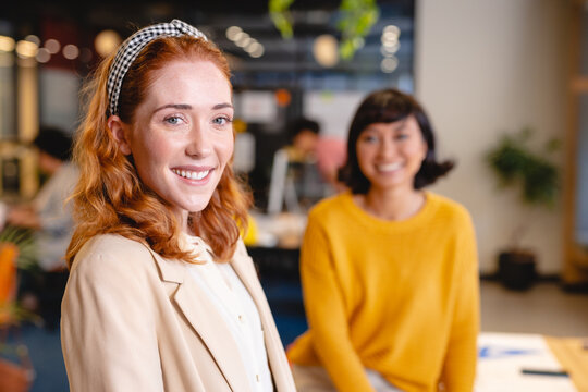 Portrait of smiling caucasian young businesswoman with female colleague in creative office