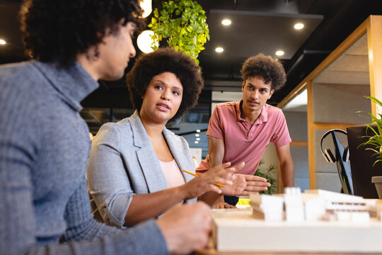 Biracial businesswoman explaining colleagues over architectural model in office