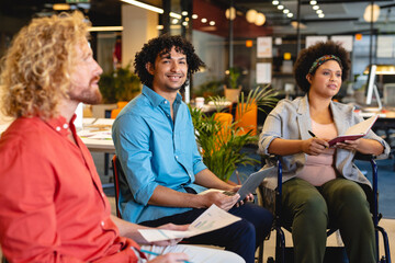 Portrait of smiling biracial businessman sitting by handicap colleague in meeting at office