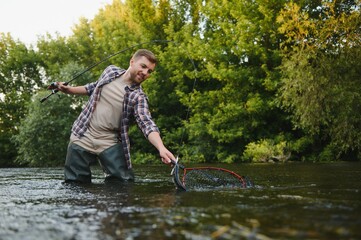 Man with fishing rod, fisherman men in river water outdoor. Catching trout fish in net. Summer fishing hobby