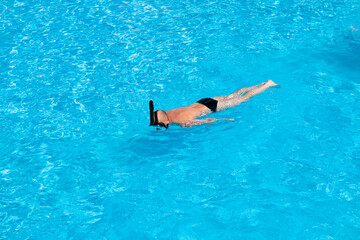 Adult man snorkeling in clear blue water on sunny day. Leisure activity concept. Lot of copy space on blue water background.
