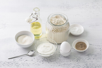Ingredients for homemade baking: egg, sour cream (yogurt), sugar, vanilla sugar, flour, vegetable oil, baking powder, salt on a light blue background