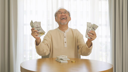 Portrait of happy rich Asian Thai old senior retired man counting money to save banknote in...