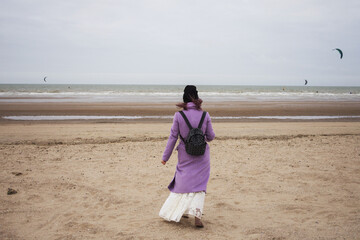 Girl in the coat and backpack walk on the beach on a cold autumn day.