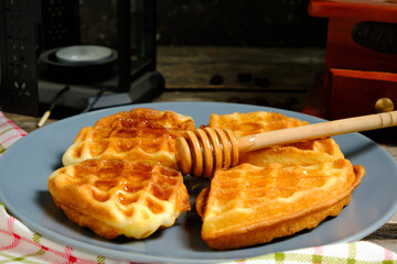 Waffles sweet pastries on plate, against background coffee grinder and decorative lamp with candle.