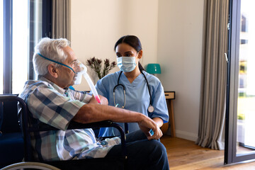 Biracial female health worker helping caucasian senior man to use oxygen mask at home