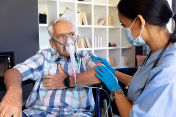Biracial female health worker helping caucasian senior man to use oxygen mask at home - Powered by Adobe