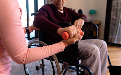 Mid section of female physiotherapist helping caucasian senior man to do exercise with dumbbells - Powered by Adobe