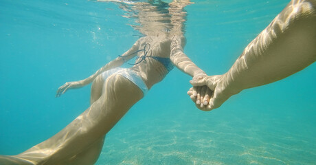 Faceless woman with beautiful body in bikini swimming underwater, holding boyfriend hand. Following...