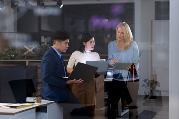 Multiracial coworkers analyzing data with laptops and report while working late in office at night