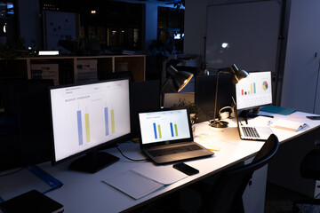 Computers with laptops, illuminated pendant lights, smartphone and diaries on desk in modern office