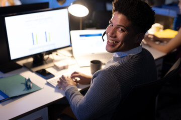 Portrait of happy male asian customer service representative wearing headset using computer on desk