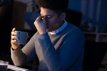 Asian businessman with head in hand holding coffee cup while working late in office at night