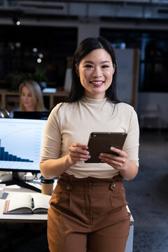 Portrait of smiling asian female professional working over digital pc in modern office at night