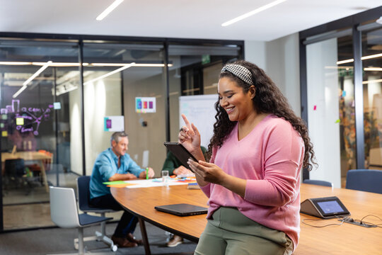 Smiling young biracial businesswoman using tablet pc while colleagues in background - Powered by Adobe