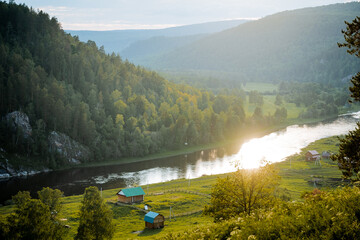A beautiful sunset glare of the sun is reflected in the river, the mountain landscape, the green...