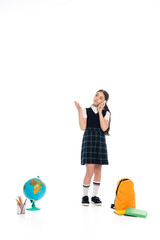 Pupil talking on smartphone and pointing with hand near globe and books on white background.