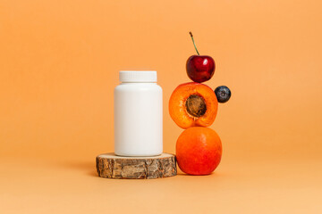 Vitamin bottle of bio supplement with fresh fruits on wooden stand. Mockup medical bottle, multivitamin, orange background - obrazy, fototapety, plakaty