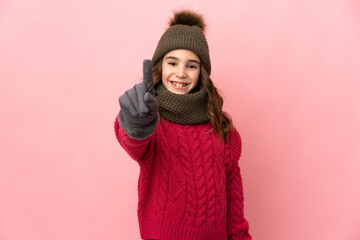 Little girl with winter hat isolated on pink background showing and lifting a finger