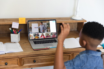 African american student raising hand while attending online class on video call over laptop at home