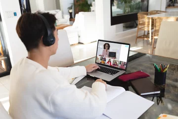 Keuken foto achterwand Aziatische plekken Aziatische tiener die een koptelefoon draagt en thuis een online lezing over een laptop bijwoont