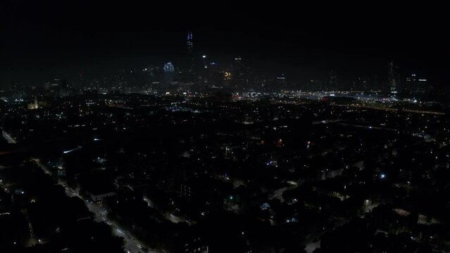 Fireworks are set off in one of Chicago's residential areas with the tall Willis Tower in the city's skyline in the background during Independence day. Backwards drone dolley shot on a clear night