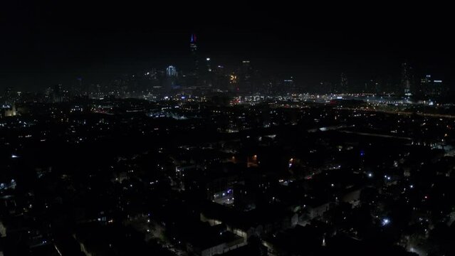 Beautiful red rockets with purple bouquets explode over one of Chicago's residential areas with the tall Willis Tower in the city's skyline in the background. Drone dolley shot on a clear night