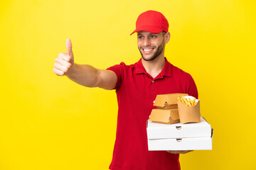 pizza delivery man picking up pizza boxes and burgers over isolated background giving a thumbs up...