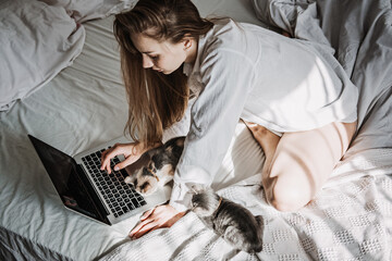 Work from home, remote online work, home office. Woman working on laptop in bed and playing with cute kitten