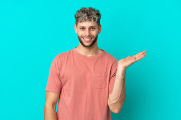 Young handsome caucasian man isolated on blue background holding copyspace imaginary on the palm to...