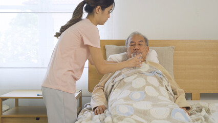 Happy woman nurse, daughter taking a medicine to sick old senior elderly patient lying on bed in...