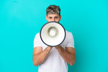 Young handsome caucasian man isolated on blue background shouting through a megaphone to announce something