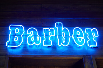 Blue neon wall sing with glowing barber inscription in loft barbershop interior, light strip