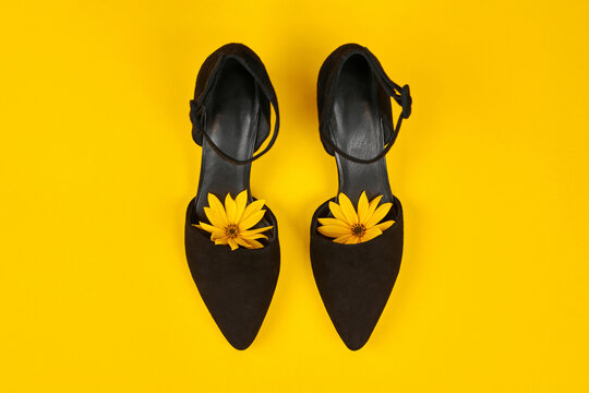 Suede black court shoes with yellow Topinambur flower bud inside toe, yellow background, womanhood