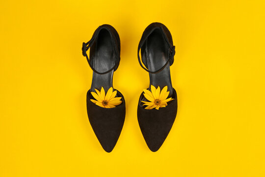 Suede black court shoes with yellow Topinambur flower bud inside toe, yellow background, womanhood