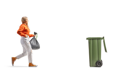 Full length profile shot of a young female carrying a plastic waste bag and walking towards a bin