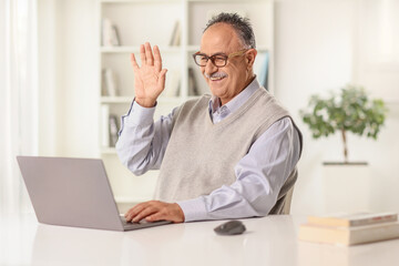 Happy mature man making a video call and waving at a laptop computer