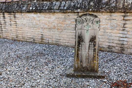 Vecchia lapide sulla tomba nel cimitero abbandonato. Sfondo con  muro in mattoncino e ghiaia.