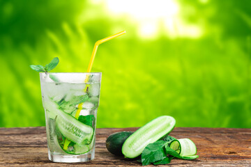 Refreshing drink with cucumber and mint, in a glass with a straw, next to ice cubes, against a green background