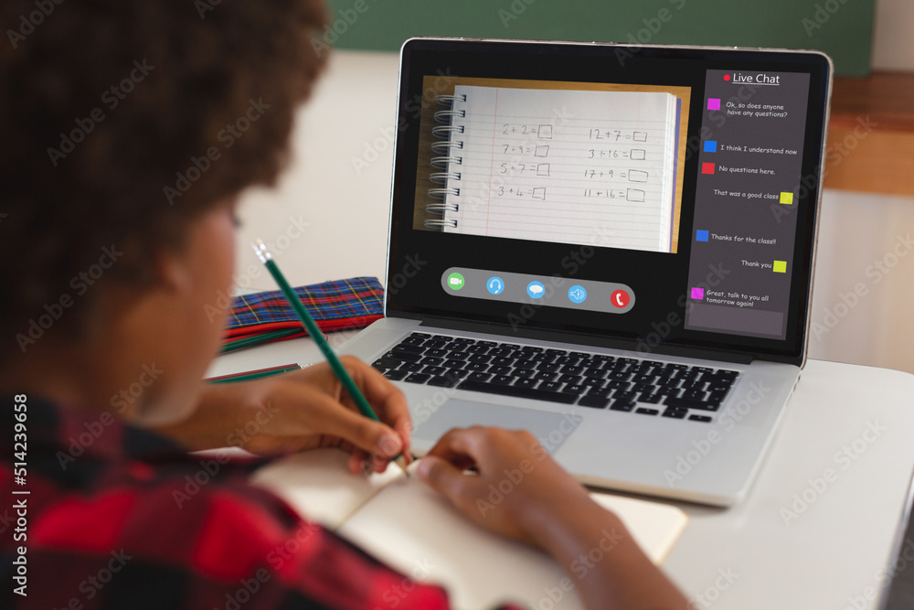 Poster African american girl with afro hair writing maths in book from laptop screen during online class