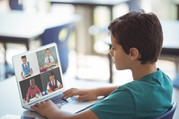 Side view of caucasian boy looking at screen with students on video call during online class at home