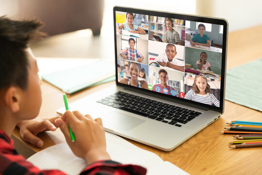 Asian focused boy looking at laptop screen with students during online class over video call at home