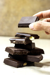 hand hold a dark chocolate almond stack, chocolate bars and block on marble background