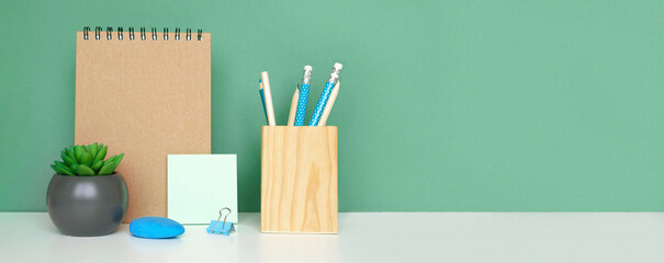School equipment on white table, green wall background. Education backdrop. Wooden school supplies,...