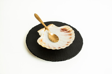 golden spoon, sea shell and a black stone tile isolated on white