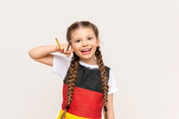 A little girl with a German flag on her T-shirt holds pencils on a white isolated background. German language courses for schoolchildren.